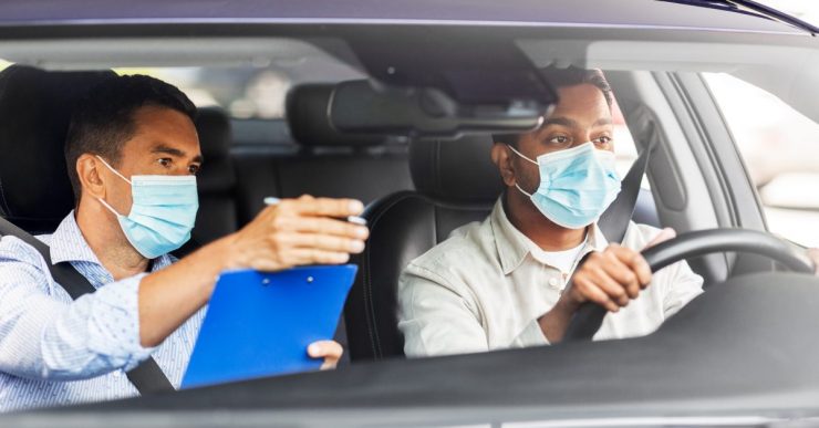 Fahrlehrer und Fahrschüler mit Medizinmaske im Auto